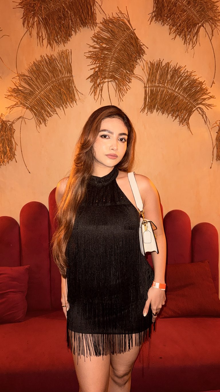 Shrestha Dutta in a black fringe dress against a scarlet velvet couch, styled for an editorial fashion portrait